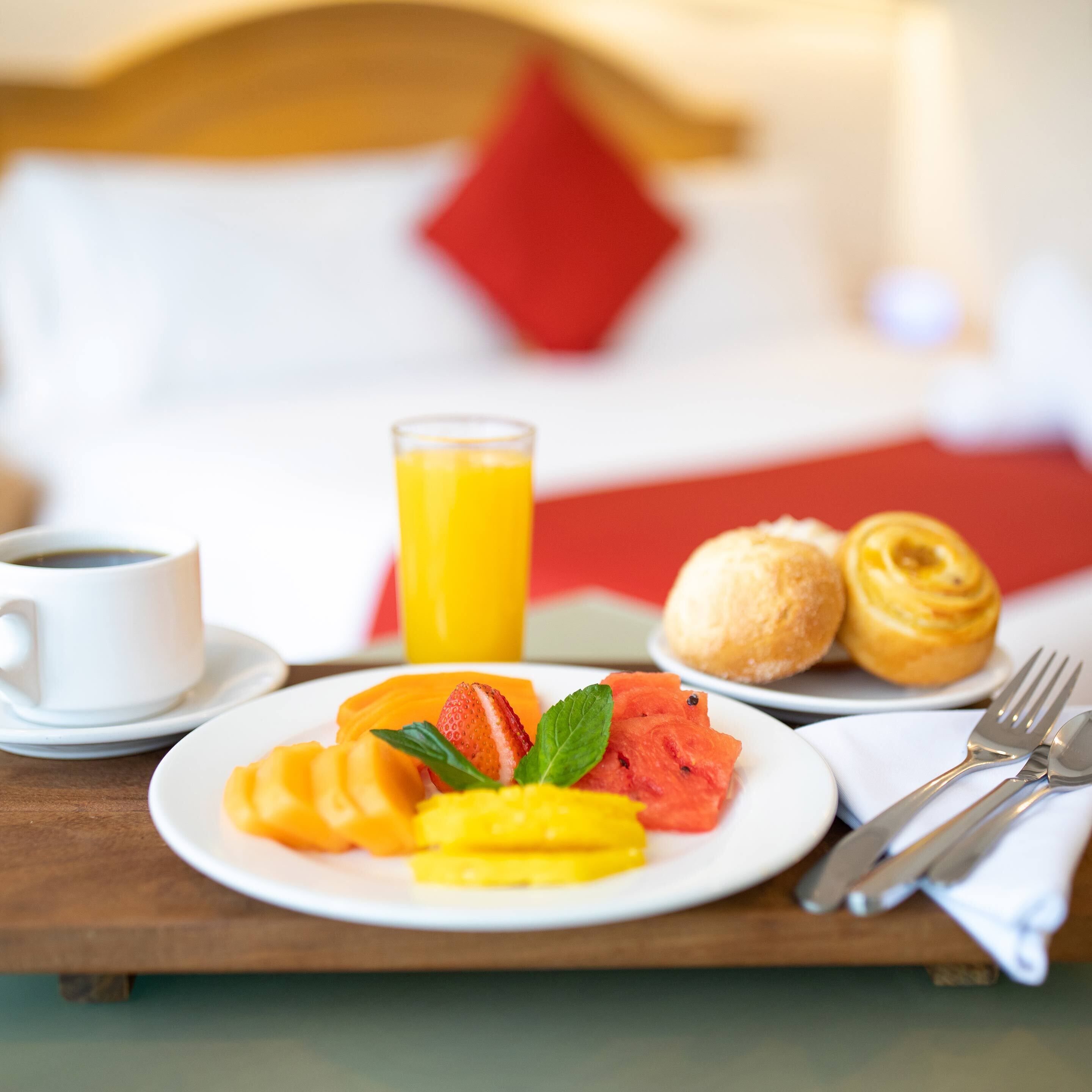A breakfast tray with sliced fruits, a glass of orange juice, croissants, and a cup of coffee on a wooden table.