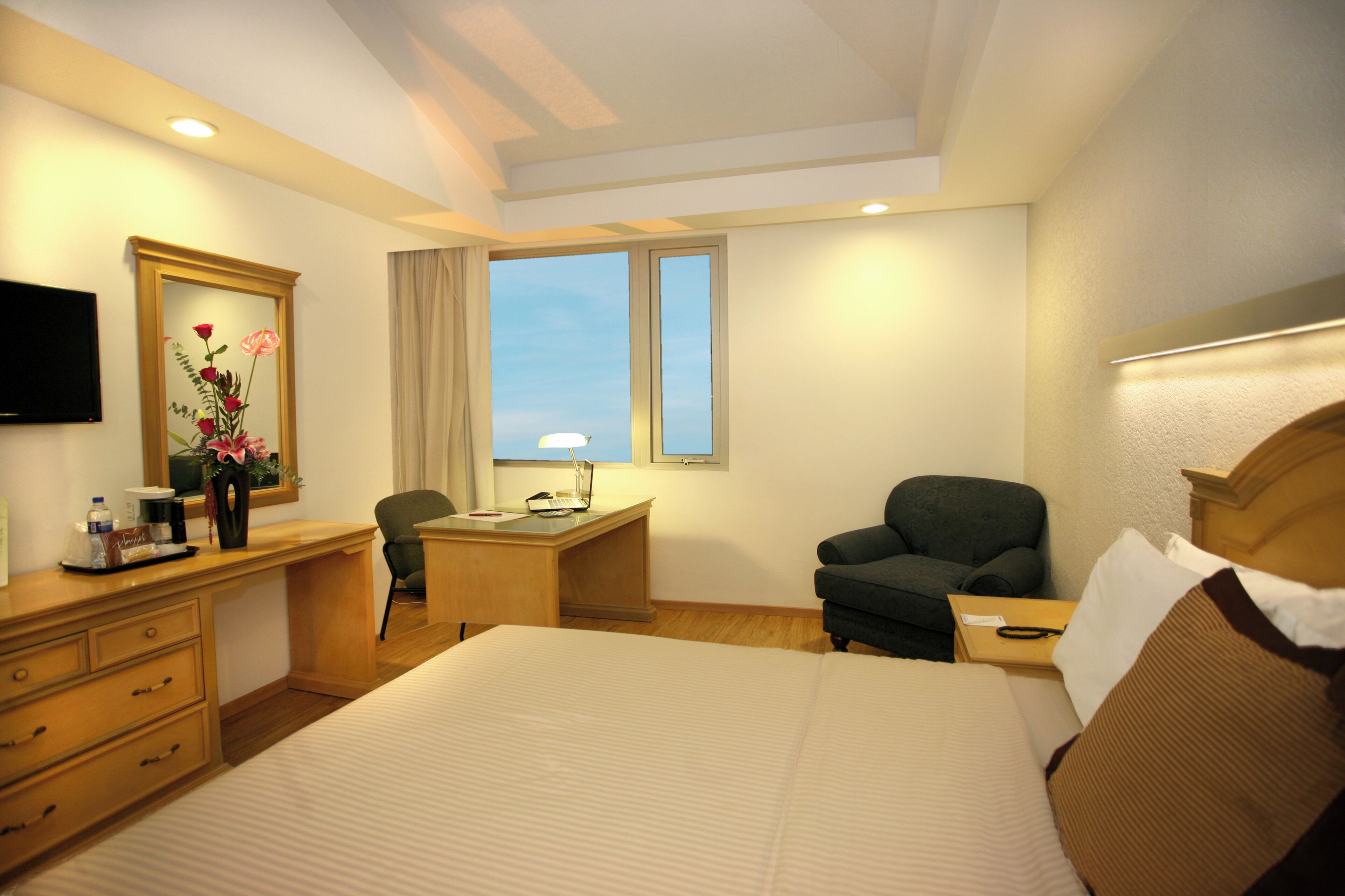 A hotel room with a bed, desk, chair, TV, and a window with curtains.