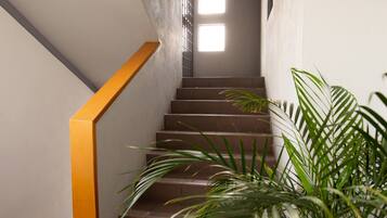 Uma escadaria com corrimão amarelo, que leva a um patamar com uma janela.