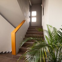 Uma escadaria com corrimão amarelo, que leva a um patamar com uma janela.