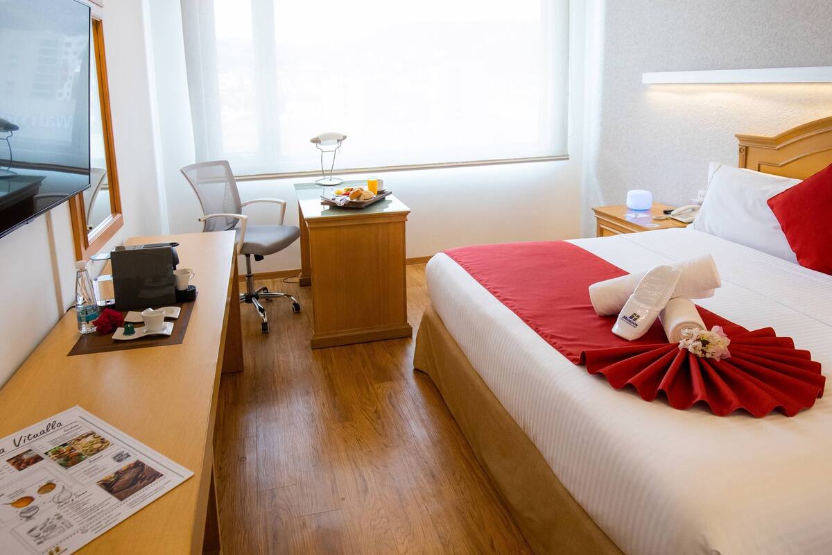 A hotel room with a bed, a desk, a chair, a TV, and a window.