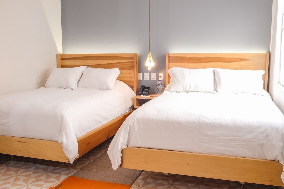 Dos camas de madera con ropa de cama blanca, una mesita de noche con teléfono y una lámpara colgante.