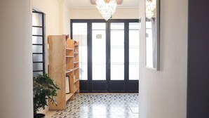 Un pasillo con piso de diseño geométrico, una estantería de madera, una planta en maceta y un par de puertas con una lámpara moderna en el techo.