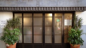 Entrada de un edificio con un amplio ventanal, dos plantas en macetas a cada lado y un letrero que dice "NUEVO LEON 120".