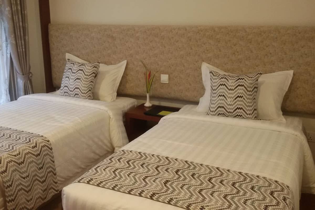 A hotel room with two beds, each with a patterned bedspread and pillows. There is a nightstand with a vase of flowers between the beds.
