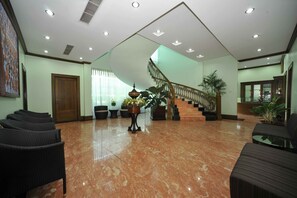 A lobby with a marble floor, a staircase, wicker chairs, and a reception desk.