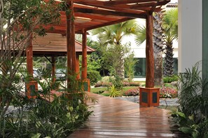 A wooden pergola with a tiled floor, surrounded by lush greenery and a variety of plants.