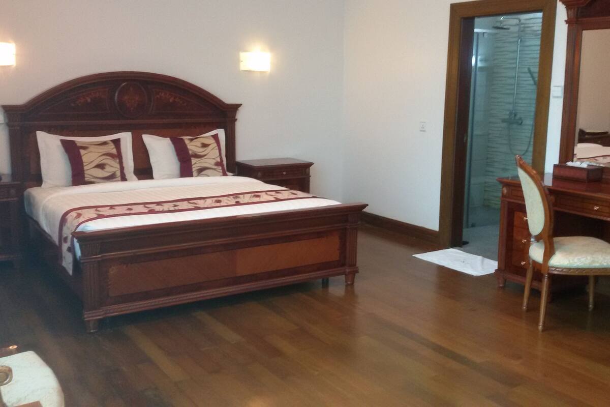 A bedroom with a wooden bed, bedside tables, a chair, a desk, and a mirror.