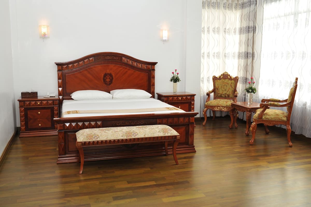 A traditional bedroom with a wooden bed, bedside tables, a bench, and two ornate chairs.