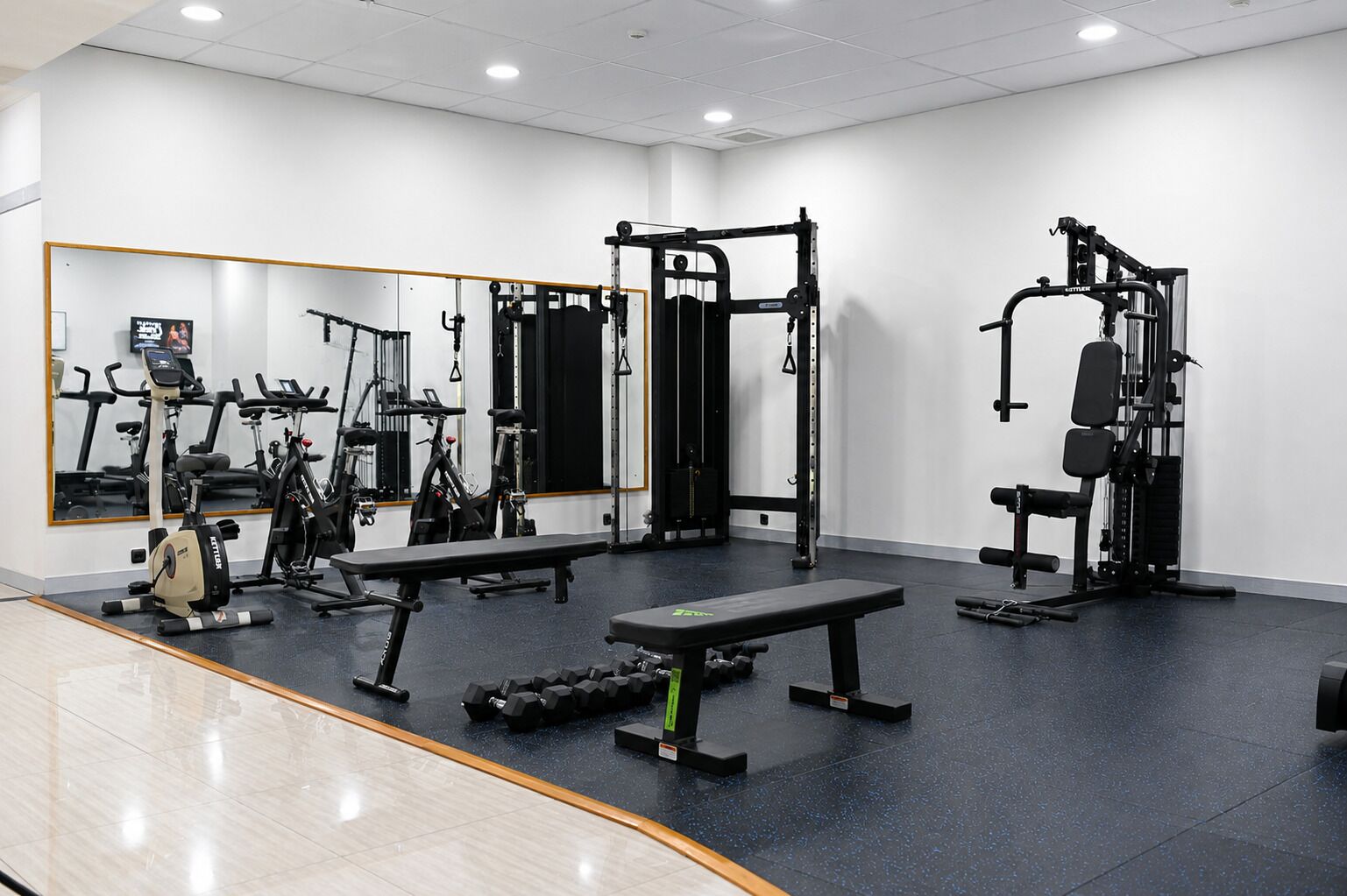 A gym with exercise equipment, a bench, and a mirrored wall.