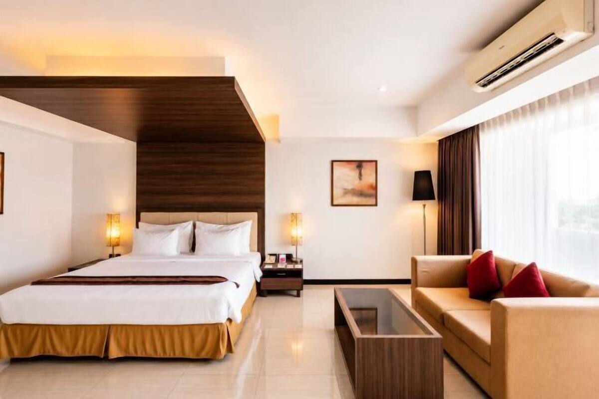 Quarto de hotel com uma cama, um sofá, uma mesa de centro e uma televisão.