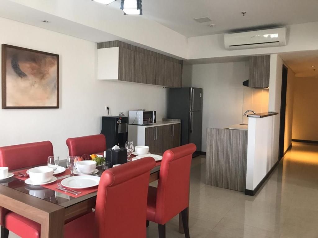 A modern dining area with a wooden table and red chairs, a kitchen with a refrigerator and microwave, and a painting on the wall.