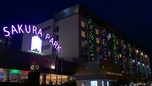 Un hôtel appelé « SAKURA PARK », doté d’un design moderne, avec une enseigne lumineuse et des éclairages décoratifs sur la façade.