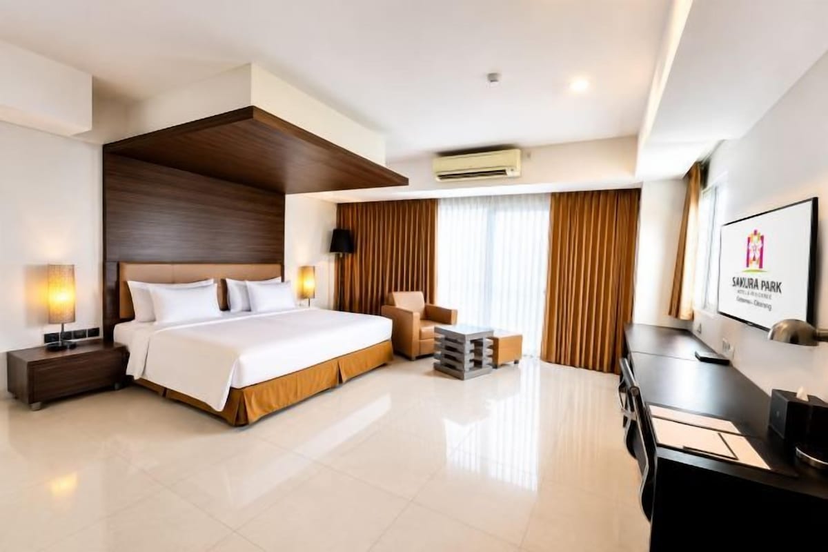 Habitación de hotel con una cama grande, mesitas de noche, un escritorio, una silla, un televisor y una ventana con cortinas.