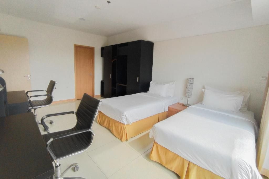 A hotel room with two beds, a desk, a chair, and a wardrobe.