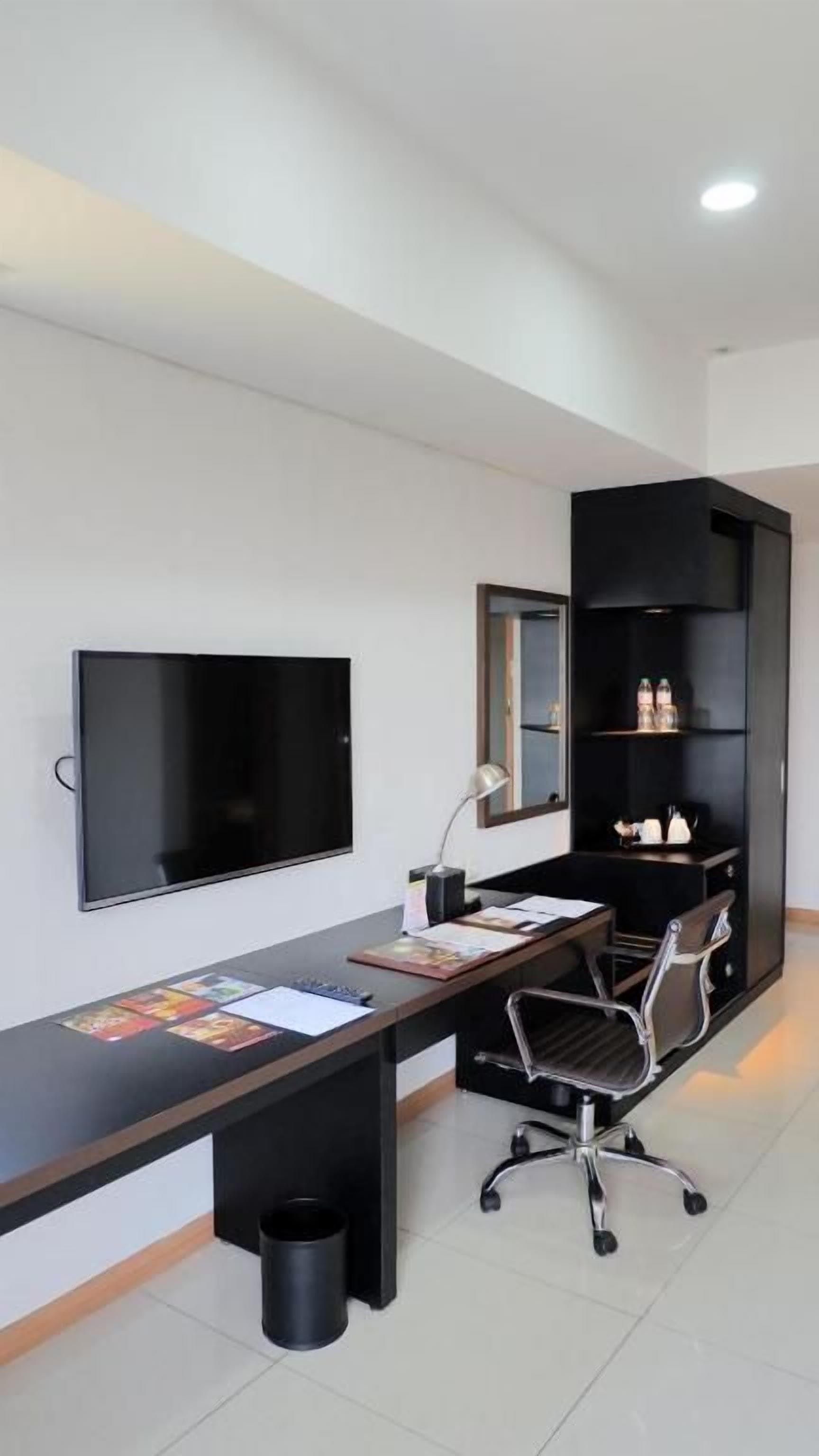 A modern office space with a long desk, a chair, a television, and a black shelving unit.