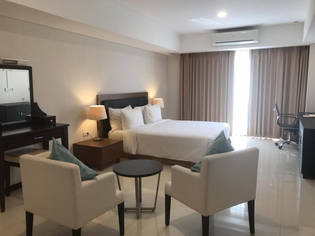 A hotel room with a bed, bedside tables, a desk, a chair, and a small round table.