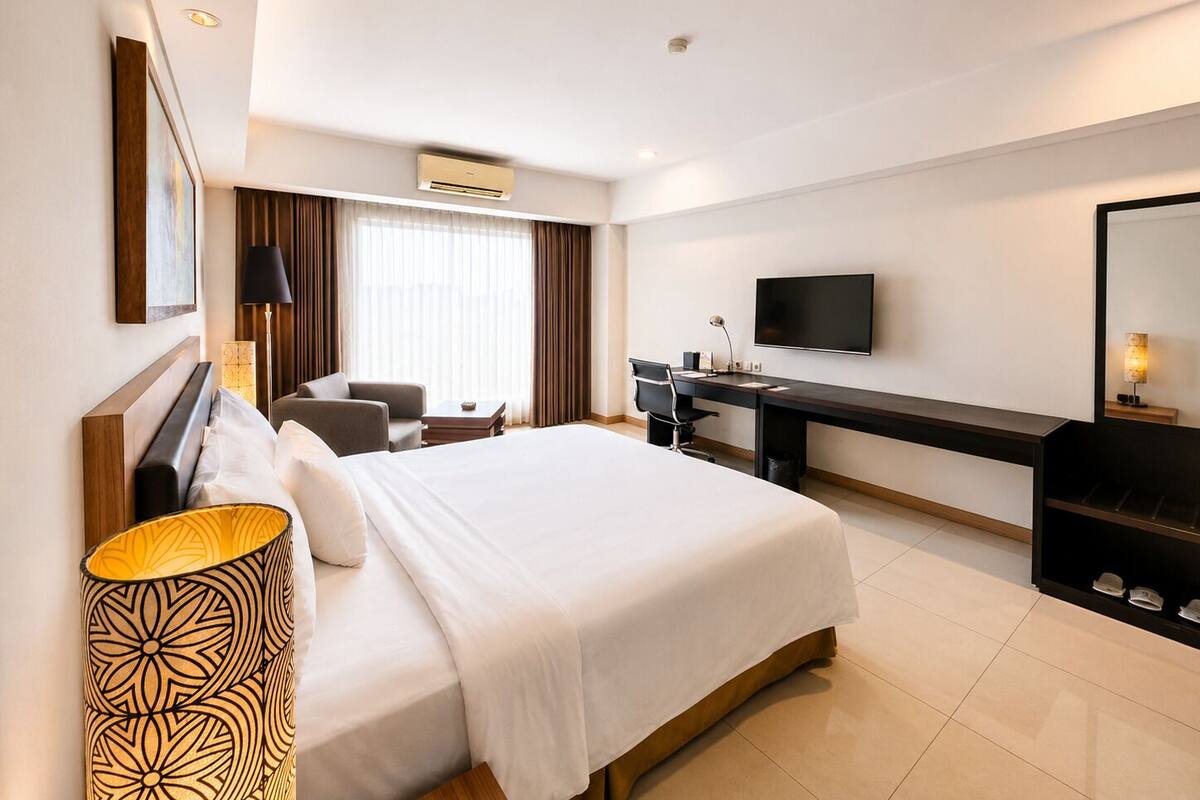 Quarto de hotel com cama, escrivaninha, cadeira, TV e uma grande janela com cortinas.