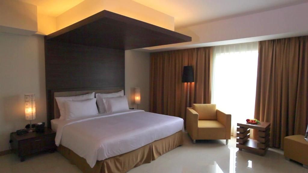 A hotel room with a large bed, a sitting area, and a window with curtains.