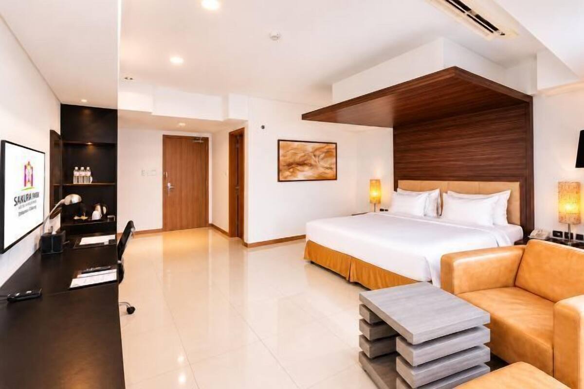 Quarto de hotel moderno com uma cama grande, uma escrivaninha, um sofá e um painel de parede em madeira.