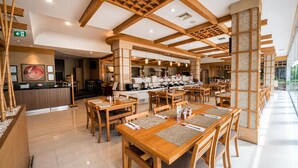 Un restaurant avec des tables et des chaises en bois, un espace cuisine et un comptoir d’accueil.