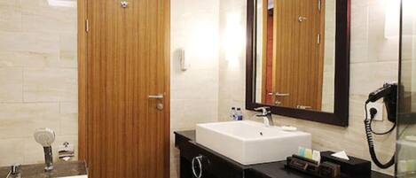 Un baño moderno con puerta de madera, lavamanos blanco, espejo grande y cabina de ducha de vidrio.