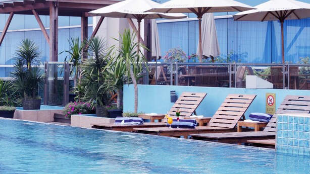 A pool area with lounge chairs and umbrellas, surrounded by plants and a covered seating area. - Java Palace Hotel (Cikarang)