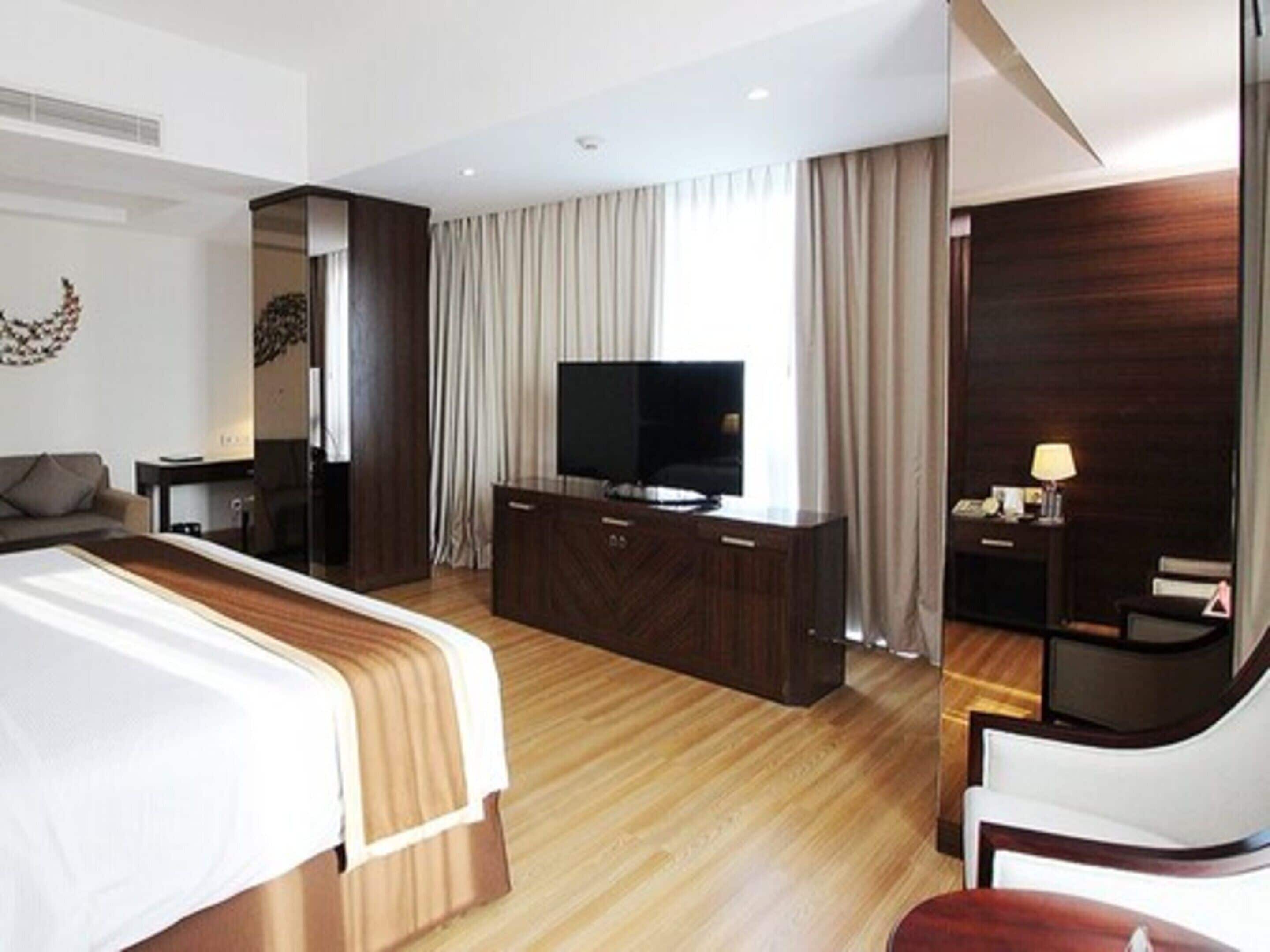 A modern hotel room with a large bed, a TV, a desk, and a chair.