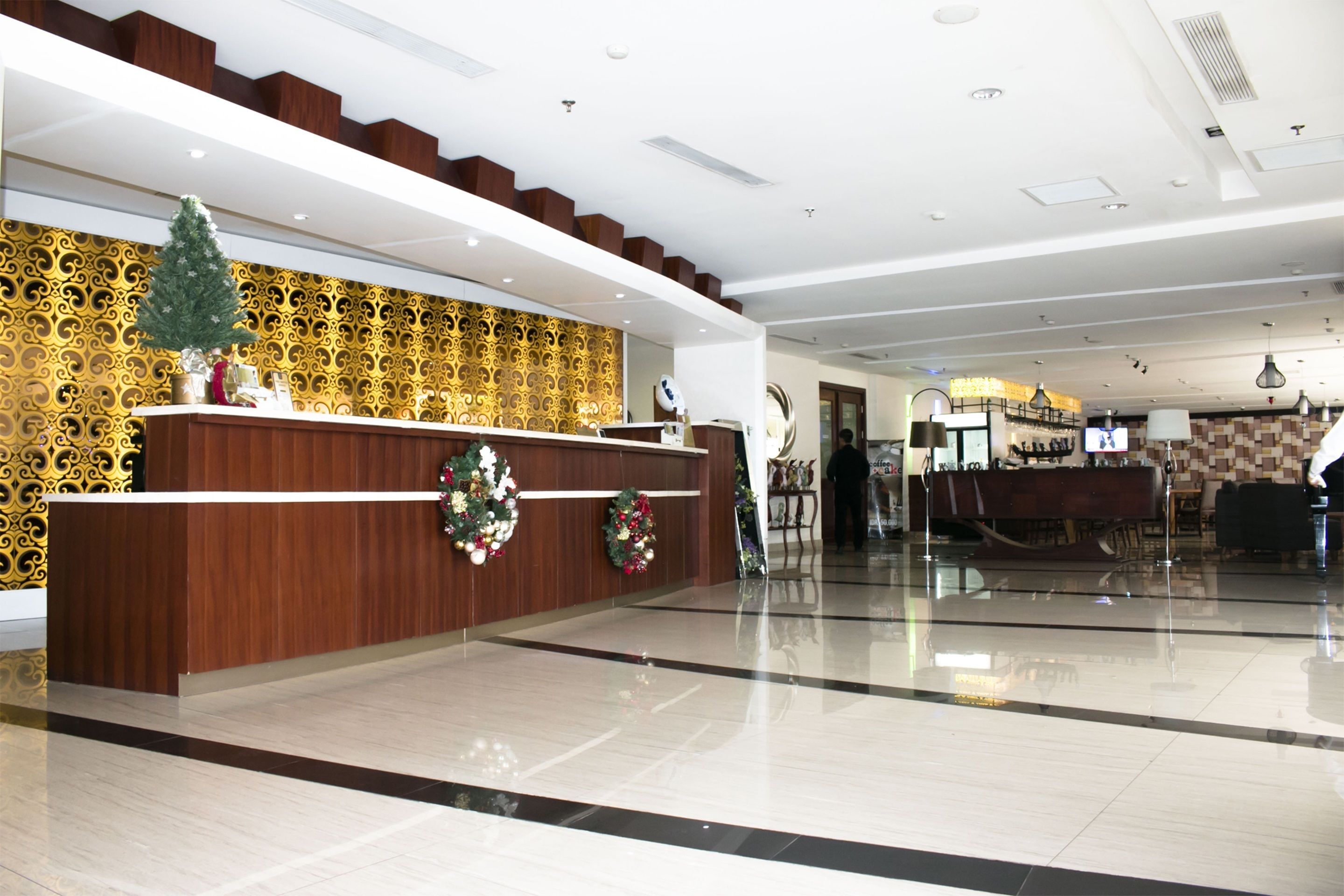 A modern hotel lobby with a reception desk, a Christmas tree, and a patterned wall.