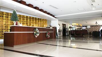 A modern hotel lobby with a reception desk, a Christmas tree, and a patterned wall.