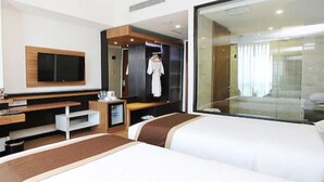 A hotel room with a large bed, a TV mounted on the wall, a wardrobe, and a glass door leading to a bathroom. - Java Palace Hotel (Cikarang)