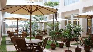 An indoor patio area with round tables and chairs, surrounded by potted plants and umbrellas. - Java Palace Hotel (Cikarang)