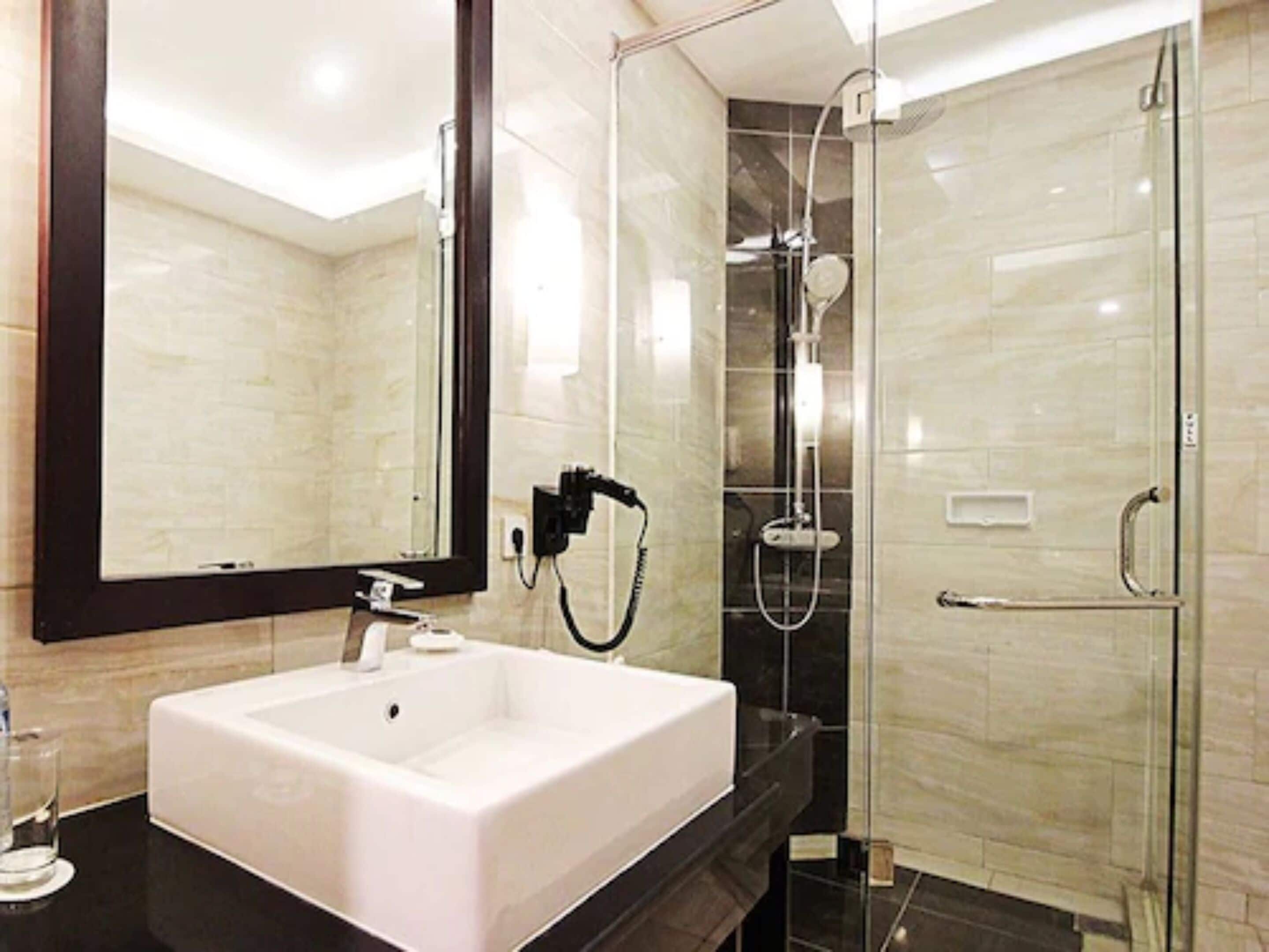 A modern bathroom with a white sink, a large mirror, and a glass-enclosed shower area.