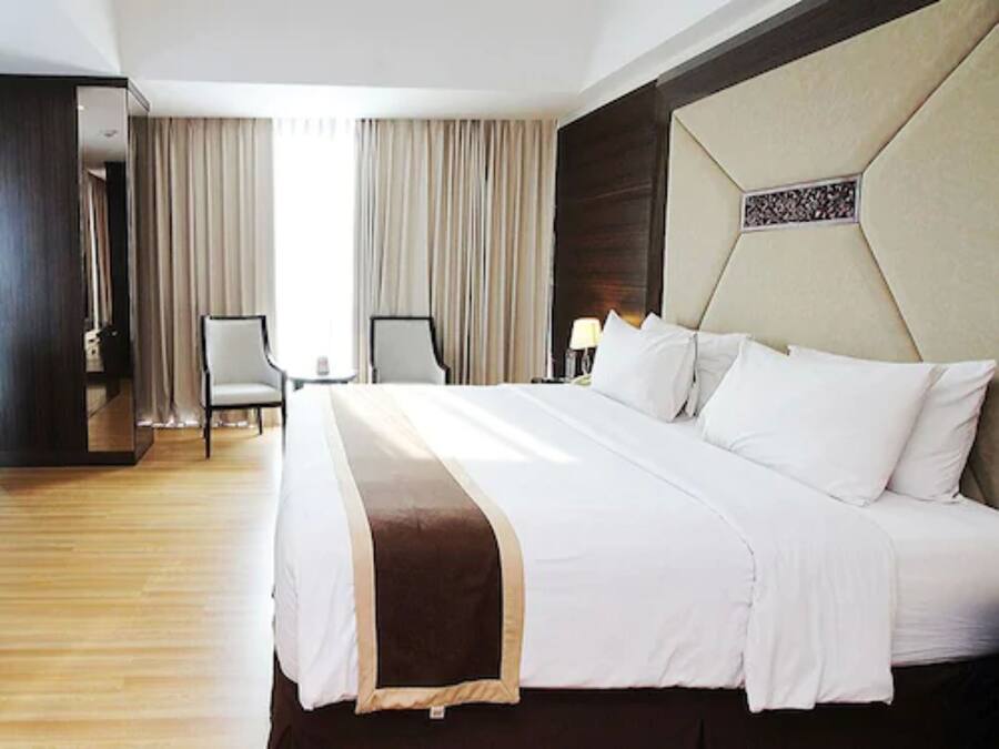 Una habitación de hotel con una cama grande, dos sillas, un escritorio y un espejo.