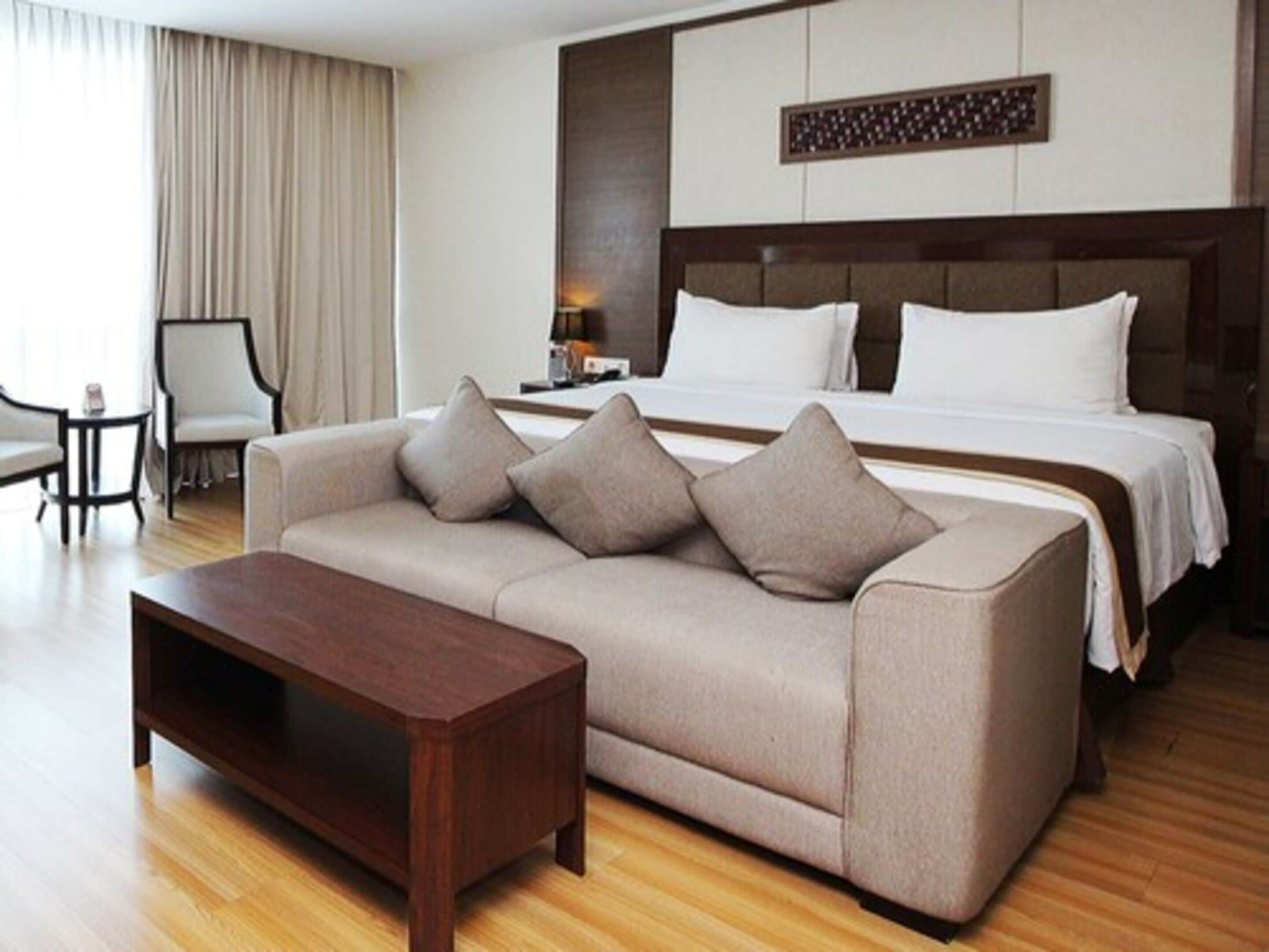 A hotel room with a bed, a sofa, a coffee table, and a chair.