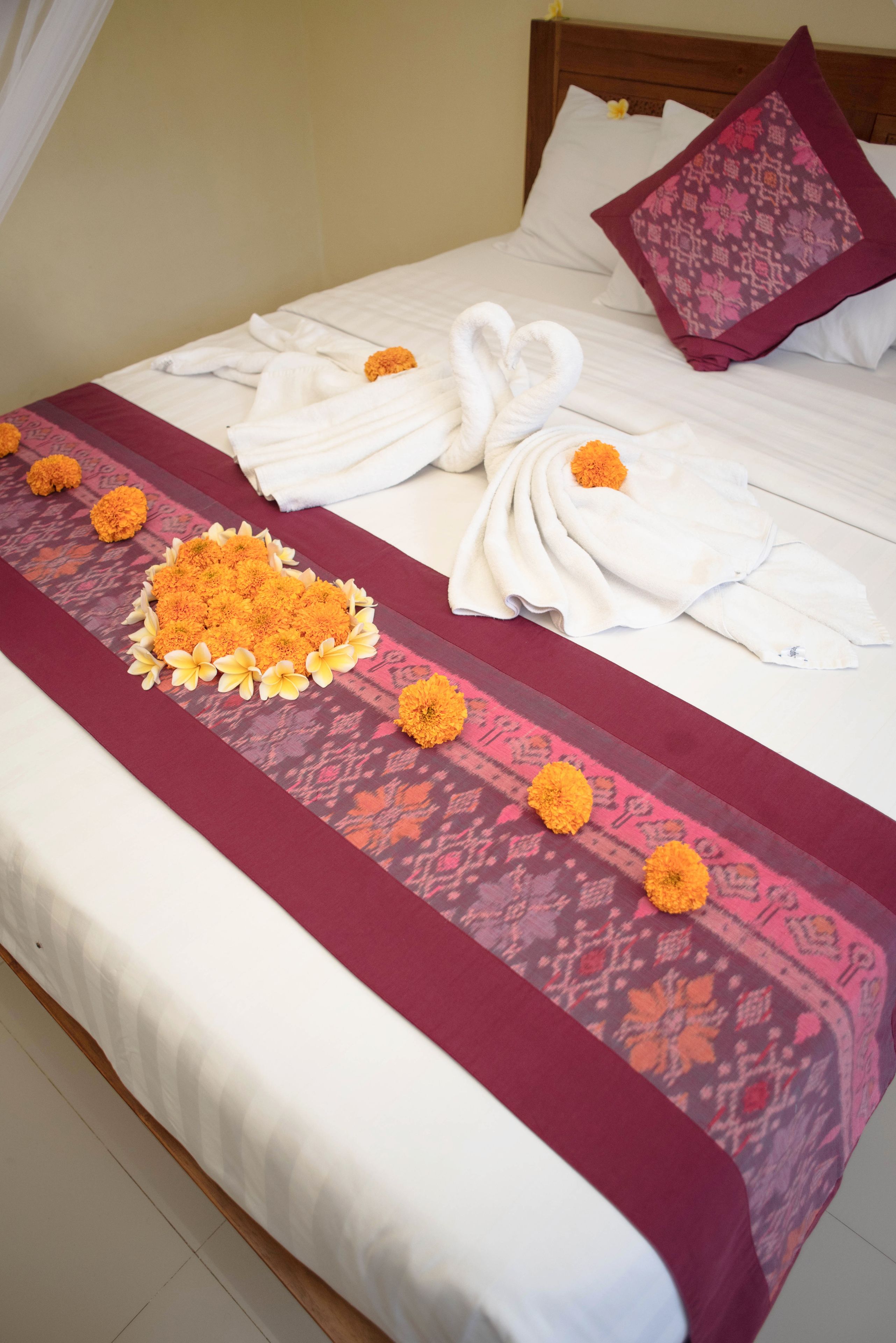 Una cama bien tendida con una colcha estampada, una decoración de toallas y un centro de mesa floral.