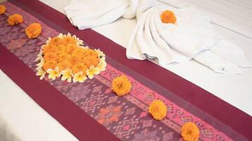 Una cama bien tendida con una colcha estampada, una decoración de toallas y un centro de mesa floral.