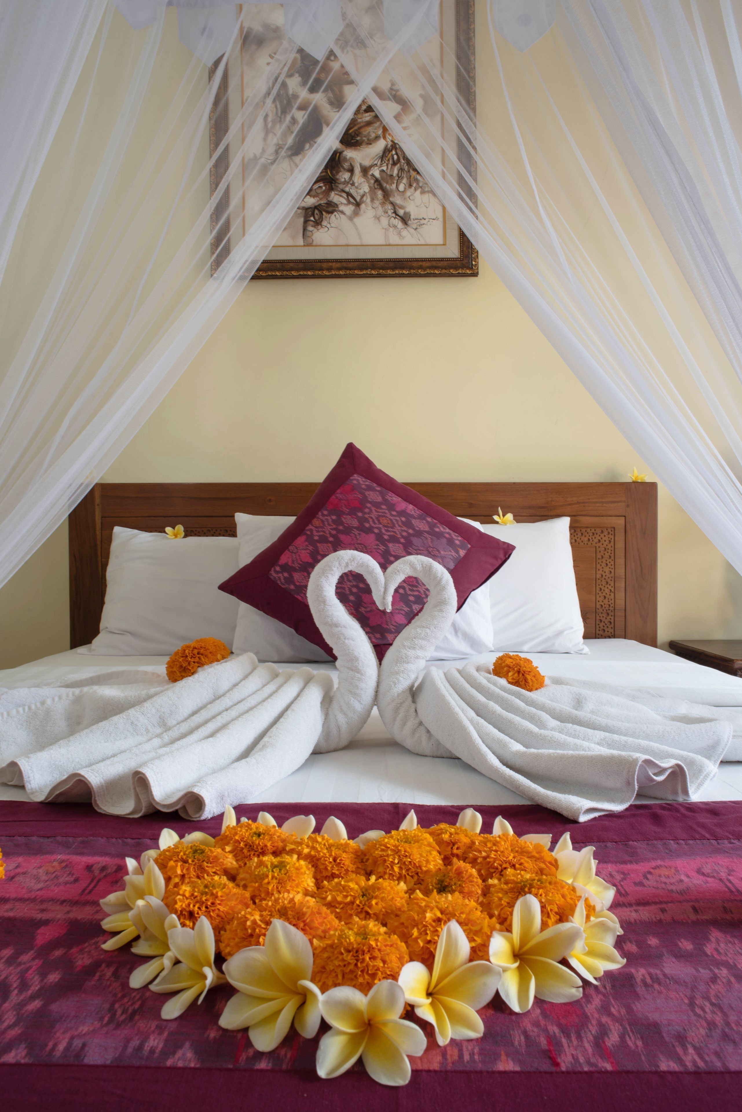 A bed with a canopy, two heart-shaped towels, and a floral arrangement.