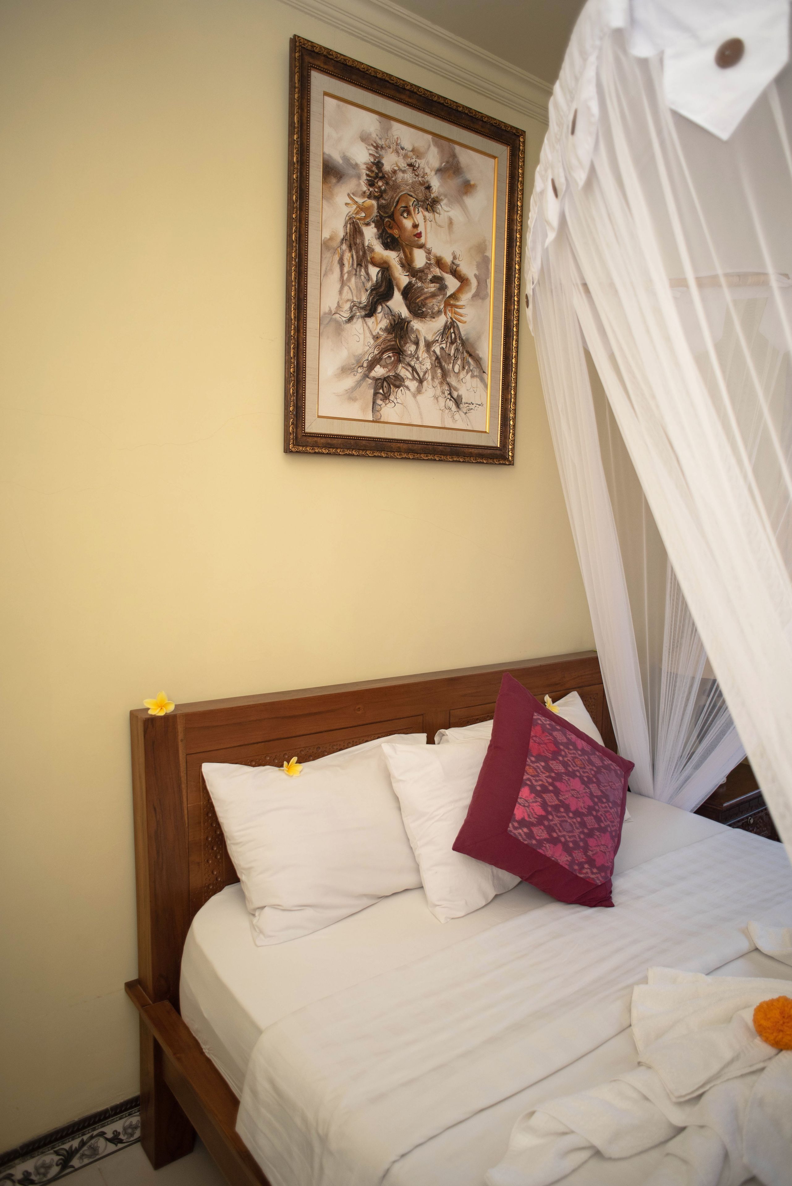 A neatly made bed with white and pink pillows, a framed artwork on the wall, and a white canopy.