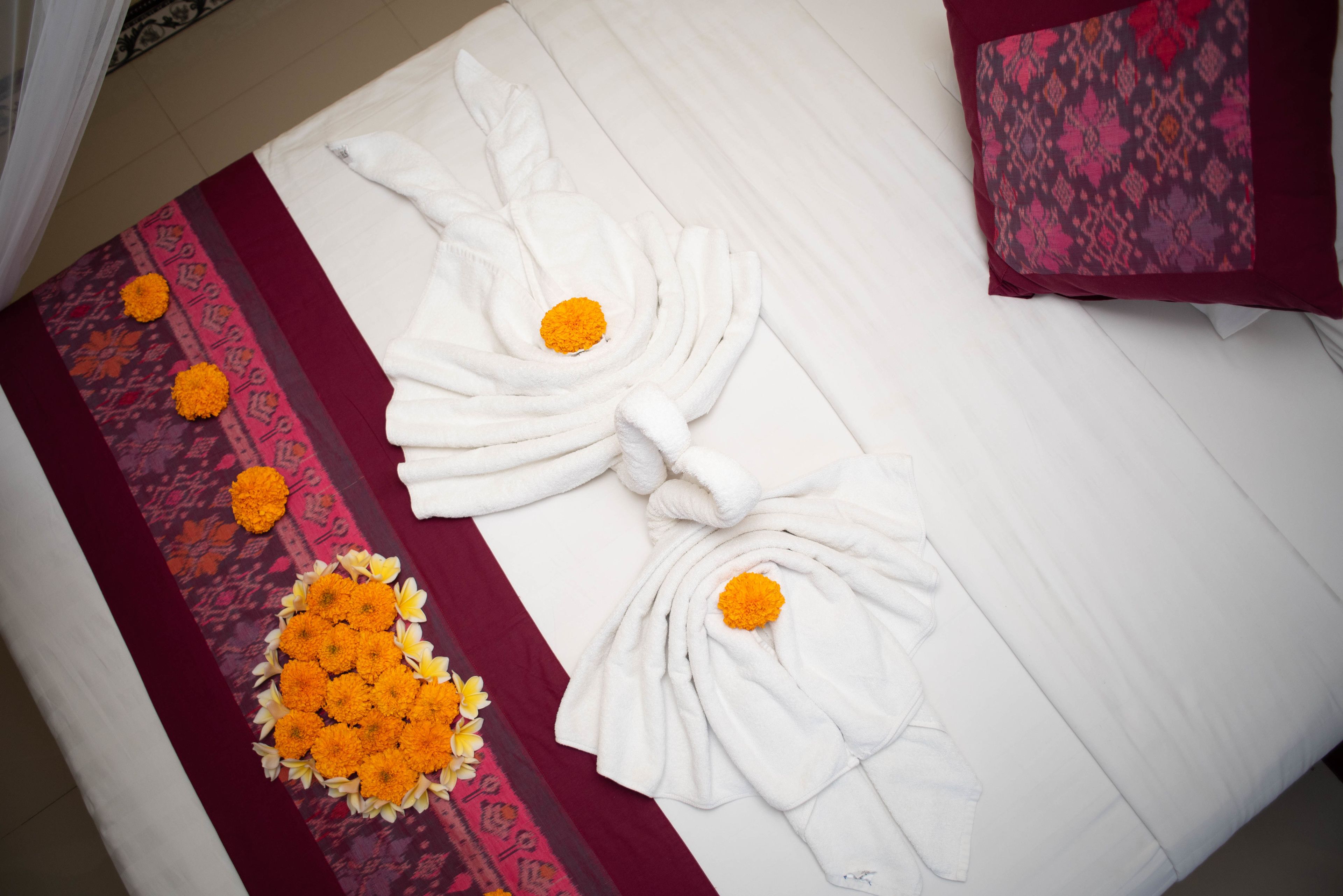 Una cama bien hecha con sábanas blancas y un arreglo decorativo de toallas con flores naranjas.