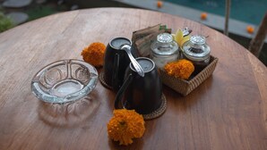Una mesa de madera con un recipiente de vidrio, una jarra negra y una cesta con flores naranjas y saleros.
