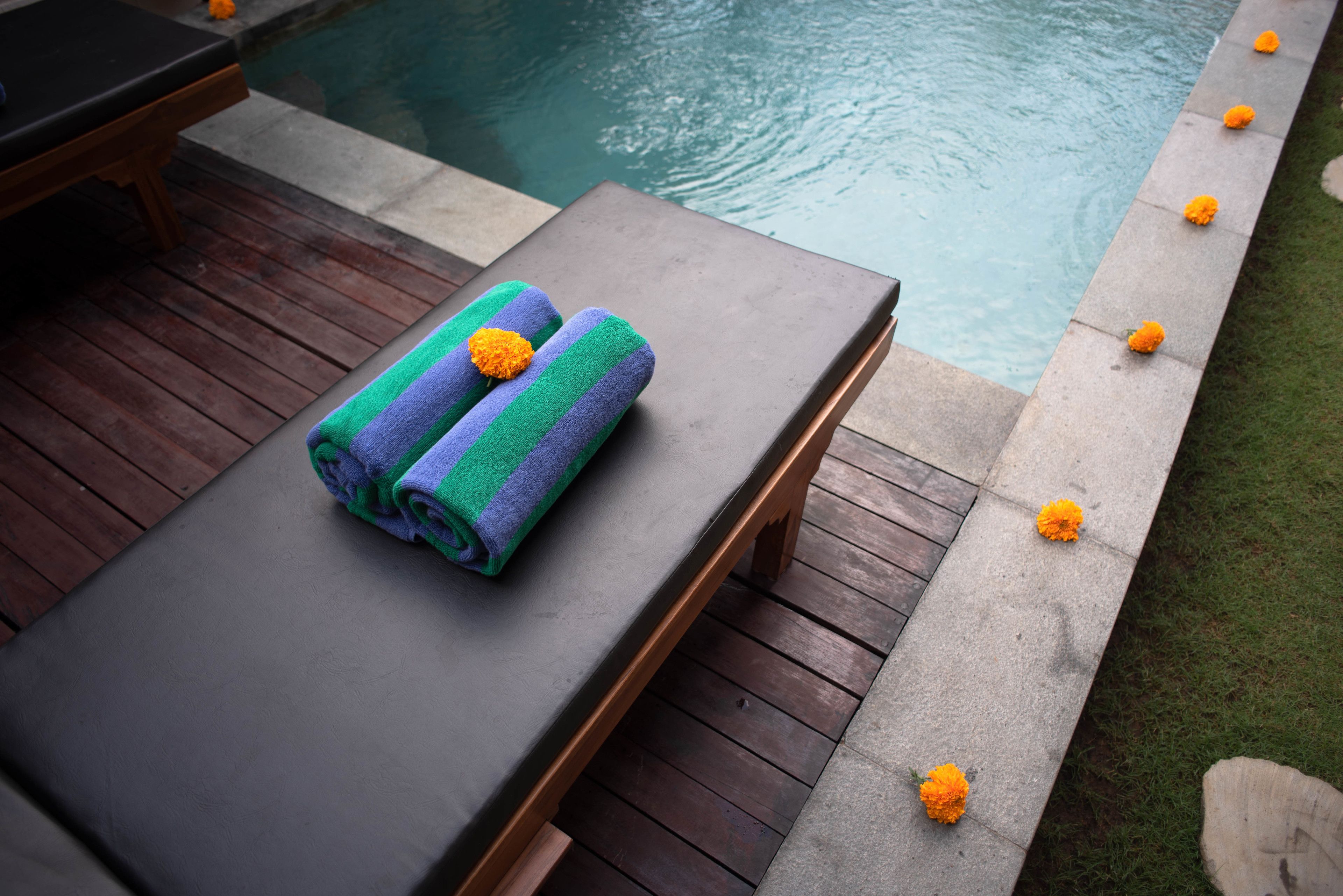 A poolside lounge area with a wooden deck and a concrete edge adorned with marigold flowers.