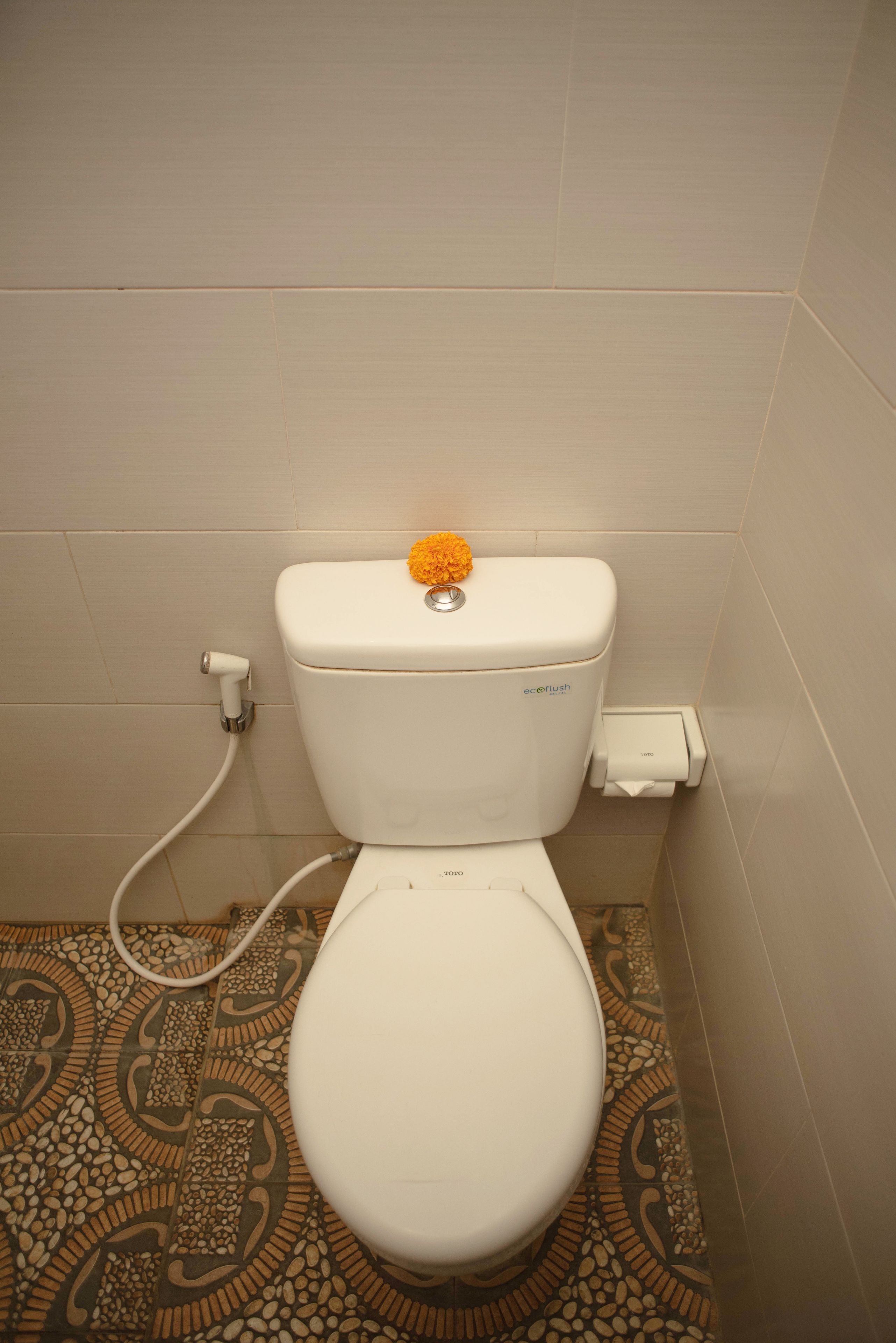 A toilet with a white seat and lid, a bidet attachment, and a patterned floor.