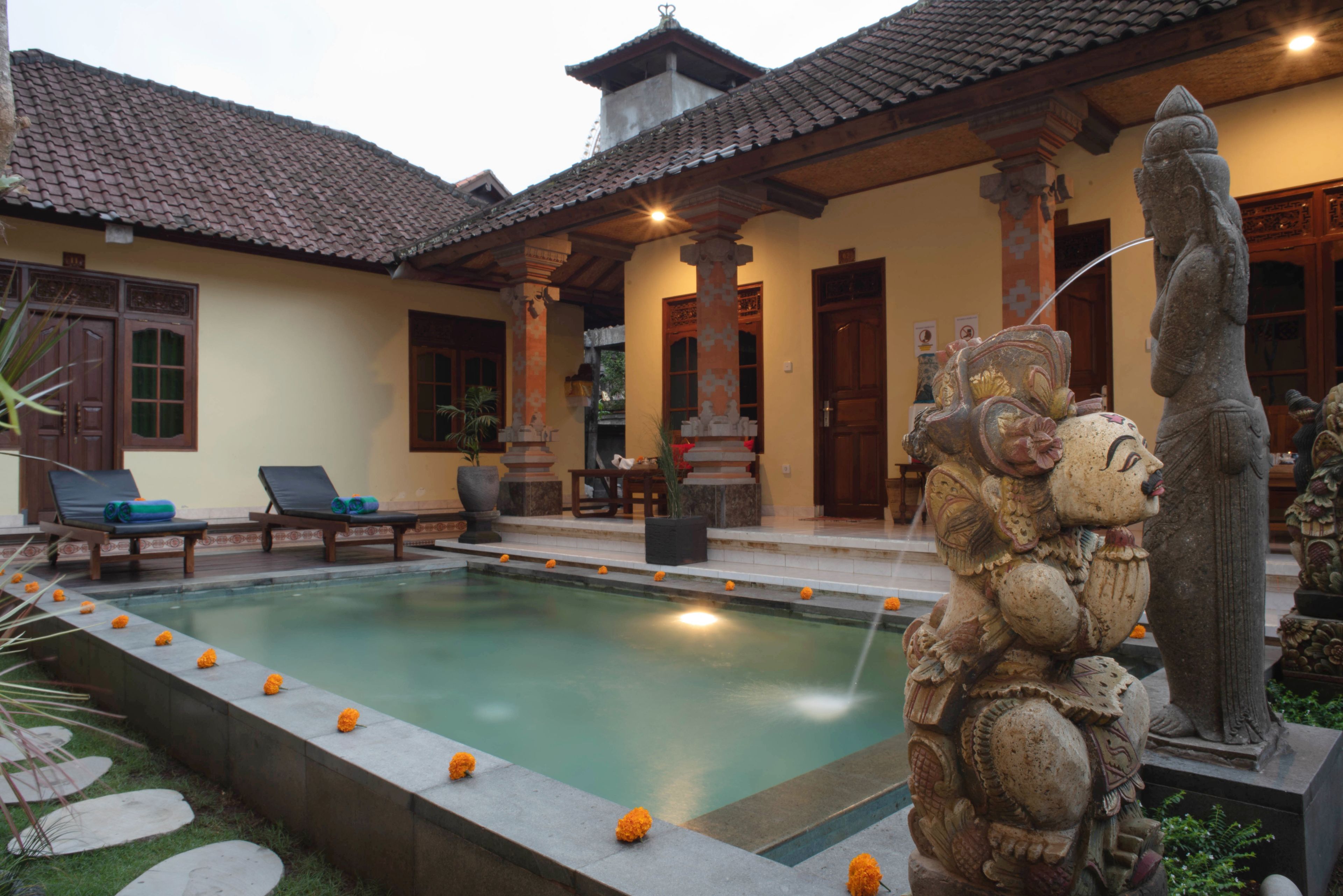 A traditional building with a swimming pool, lounge chairs, and a statue.