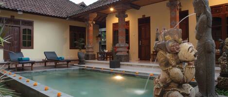A traditional building with a swimming pool, lounge chairs, and a statue.