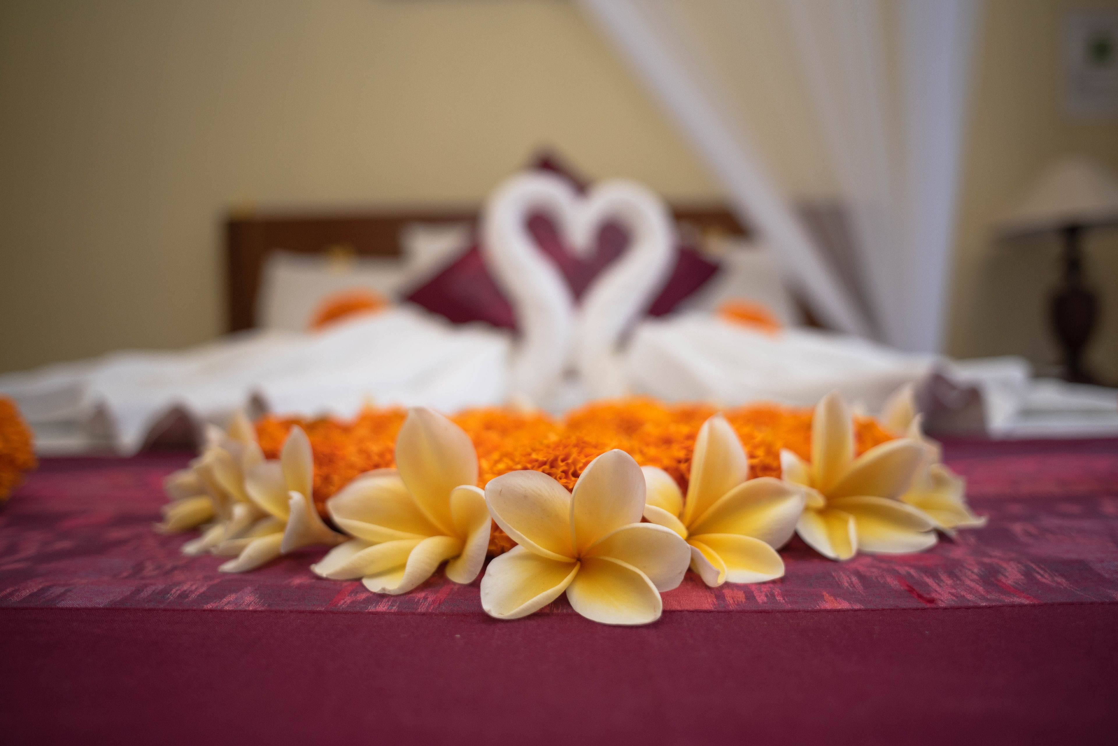 A bed with a red bedspread, white pillows, and a heart-shaped decoration made of white flowers.