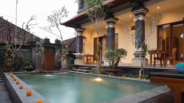 Un patio tradicional con piscina, estatuas de piedra y mobiliario de madera.