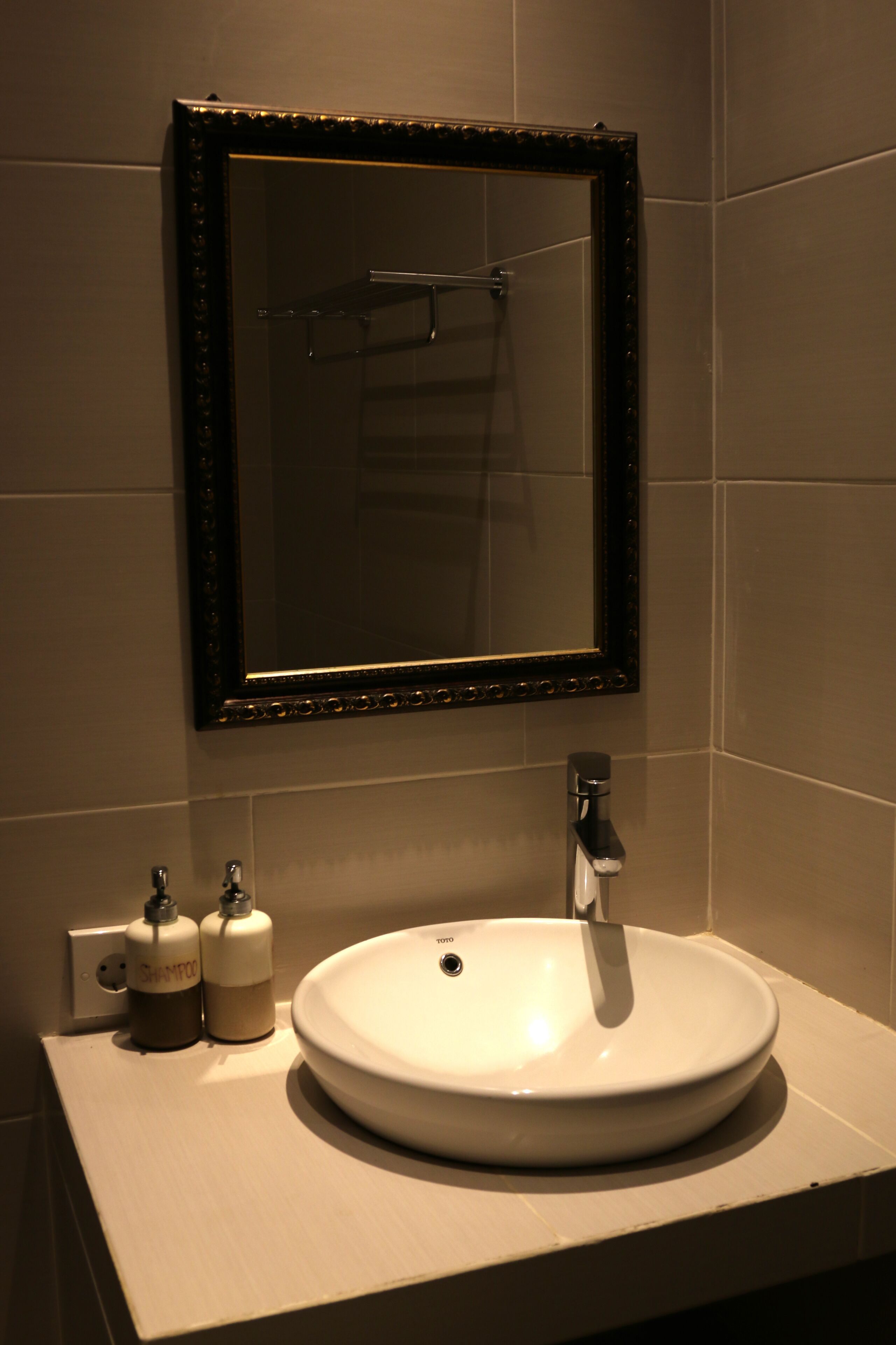 A bathroom with a white sink, a mirror with a dark frame, and two bottles of shampoo.
