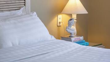 A hotel room with a bed, a nightstand with a lamp, a book, and a framed artwork on the wall.