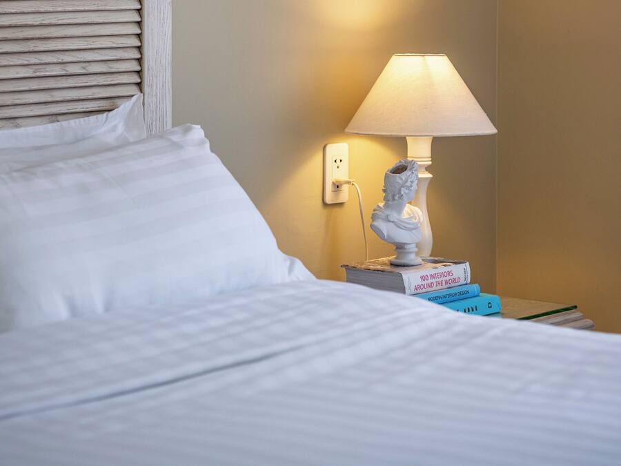 A hotel room with a bed, a nightstand with a lamp, a book, and a framed artwork on the wall.